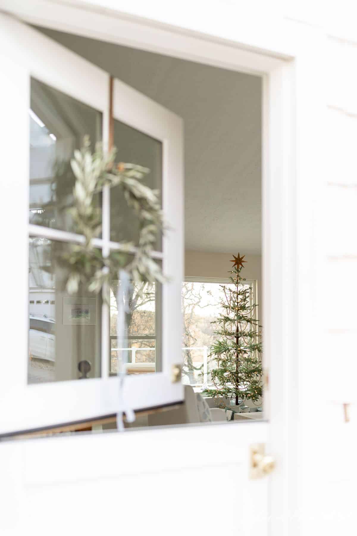 一扇荷兰式门的窗户上挂着一个自制的花环，可以看到为圣诞节装饰的客厅。