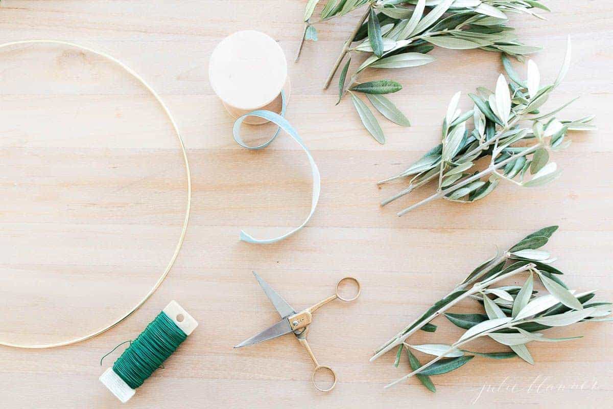 一张带金箍的木桌。剪刀、铁丝、缎带和绿色植物摆好用来做花环。