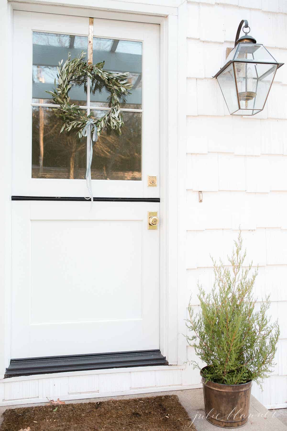一个手工制作的小橄榄花环挂在白色荷兰门的上半部分，旁边是一棵小圣诞树。
