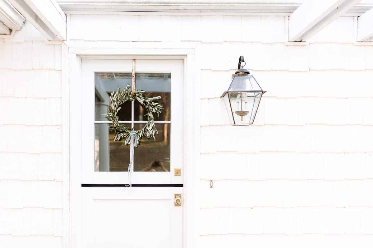一座白色房子的入口，有一扇荷兰式的门，上面挂着自制的橄榄花环。