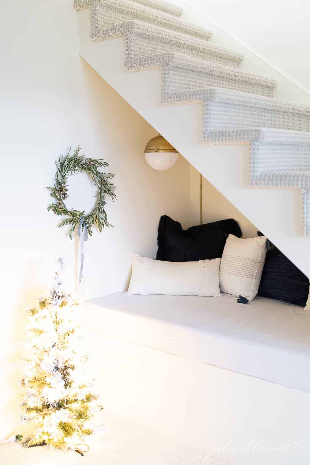 一个自制的圣诞花环挂在楼梯下的角落里，上面堆着蓝色和白色的枕头。