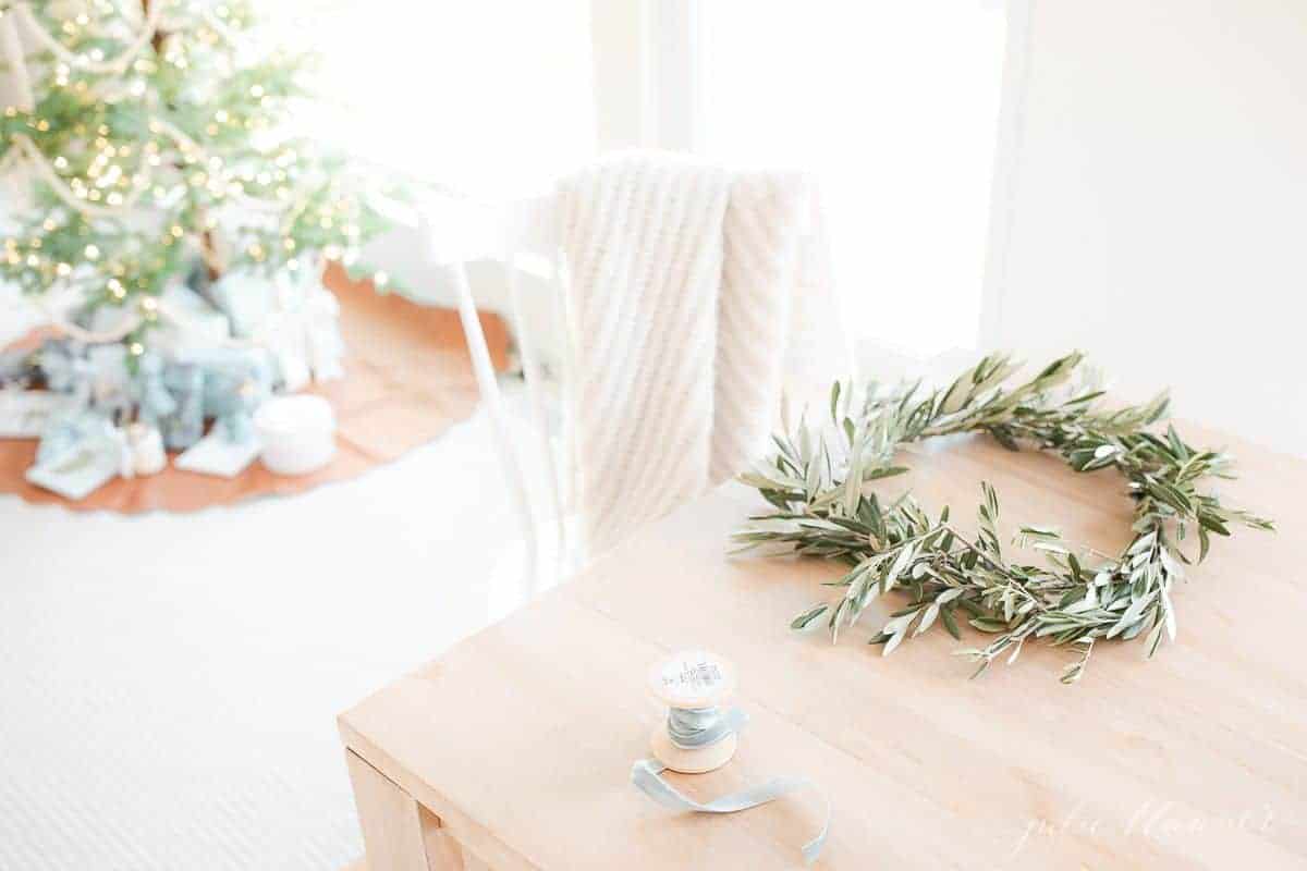 木制桌子上有一个手工制作的小橄榄花环，背景是圣诞树。