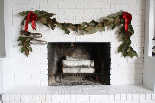 白色的壁炉上挂着红丝带和冰鞋的花环。