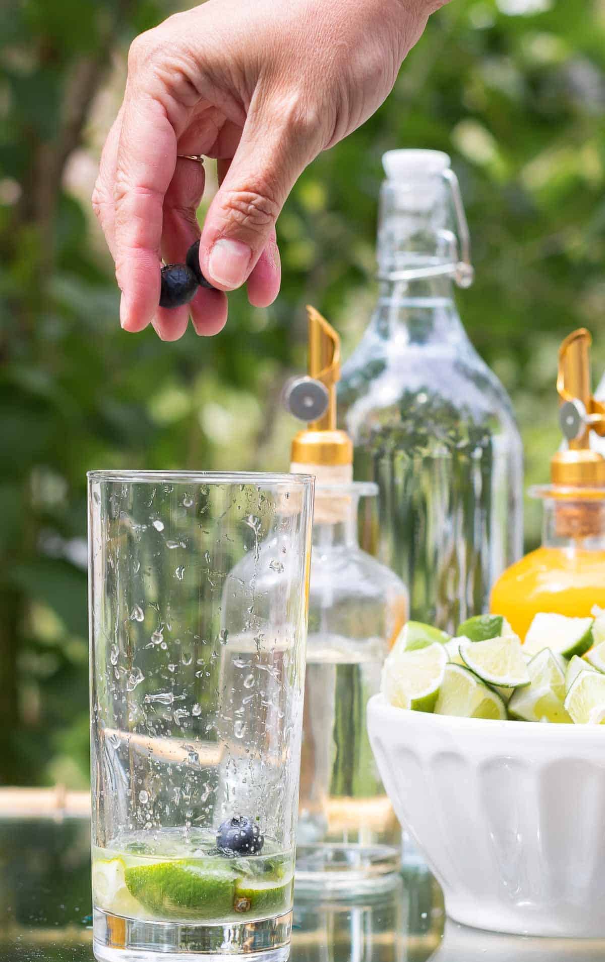 在金色和玻璃酒吧推车上设置了一个莫吉托酒吧，一只手伸手将蓝莓放入玻璃杯中。