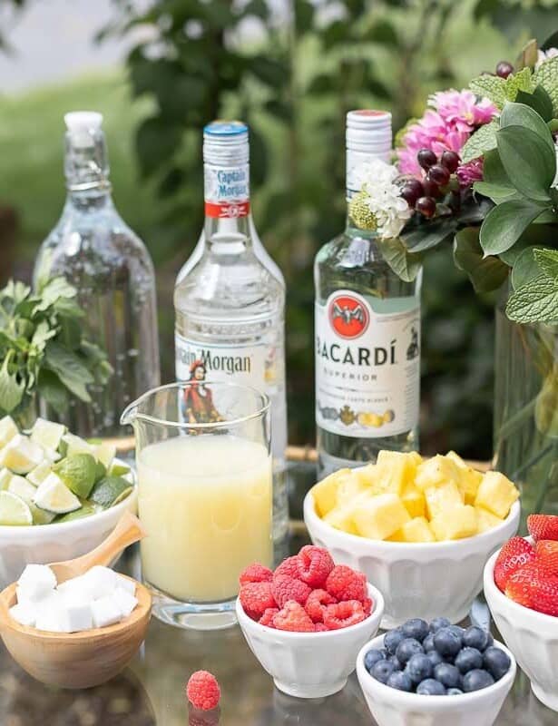 玻璃和黄铜酒吧推车与莫吉托酒吧户外，各种各样的水果和石灰在碗旁边酒精瓶旁边。