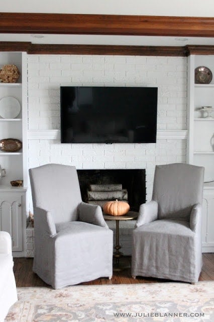 一个带有白色彩绘砖砌壁炉的客厅，电视拿着壁炉架隐藏电视绳。
