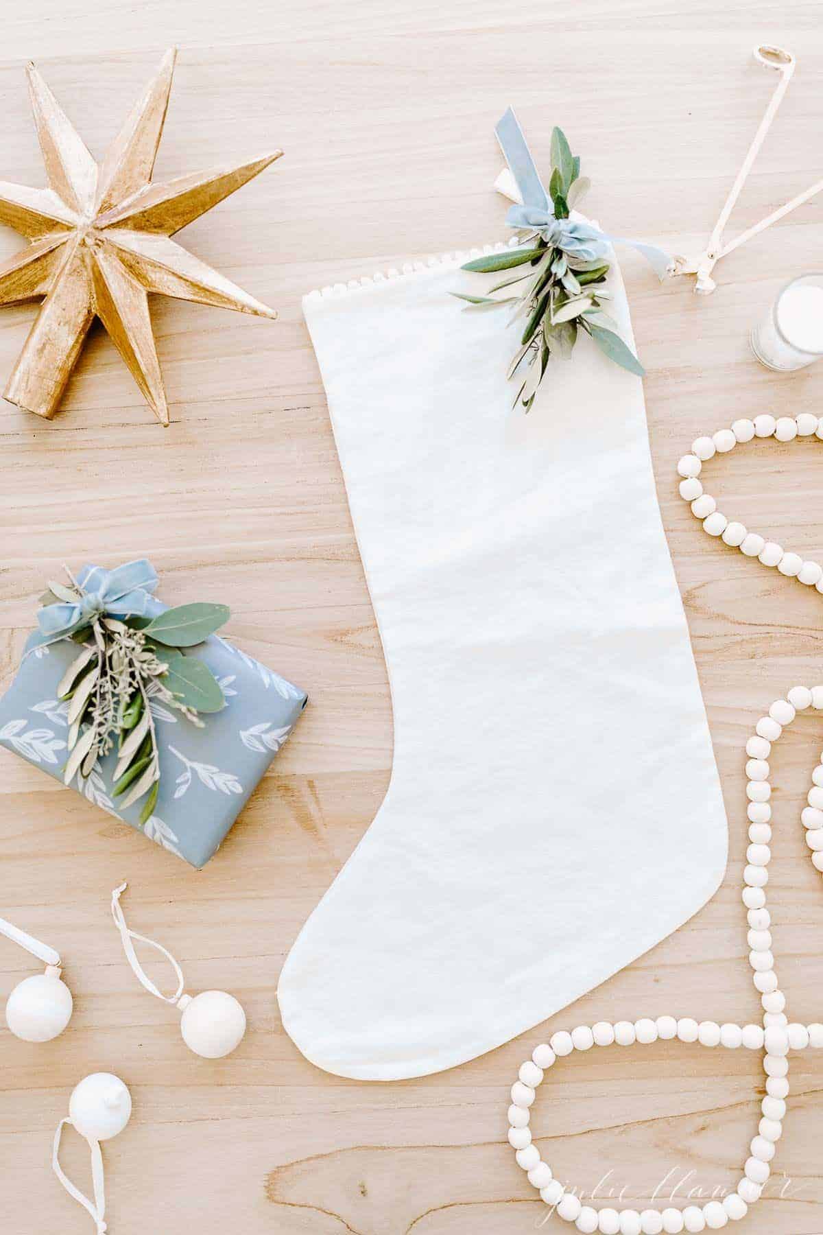 一个木制表面与亚麻长袜，礼品卡在一个蓝色包装的盒子，和木制圣诞装饰品周围。