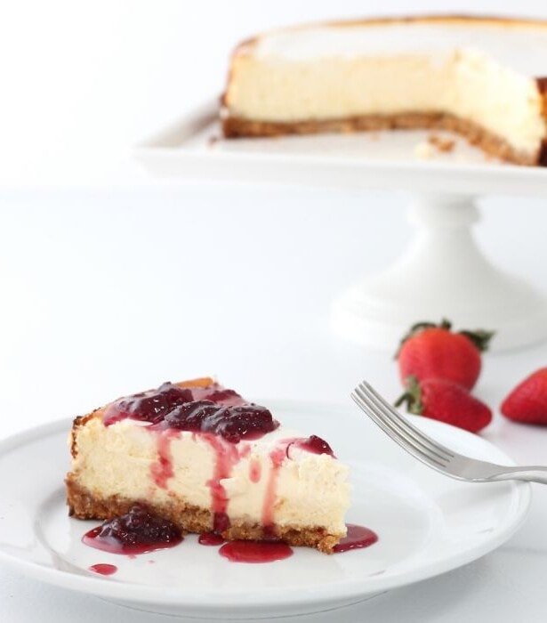 草莓芝士蛋糕放在白盘子里。草莓和一个饱满的蛋糕在旁边。