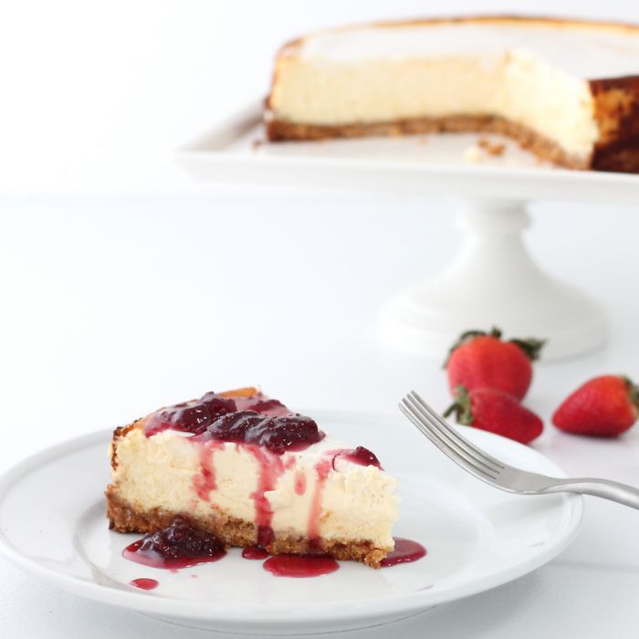 白色盘子里的草莓芝士蛋糕。草莓和一个完整的蛋糕放在一边。gydF4y2Ba