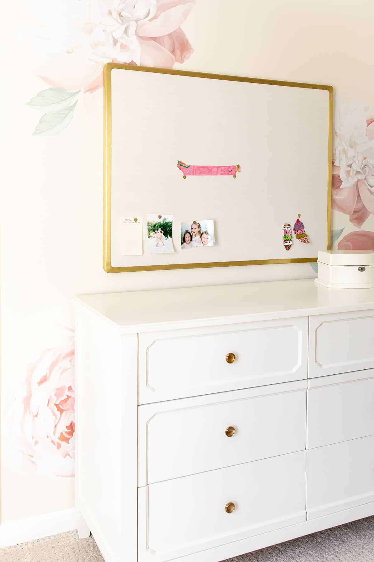浅粉色和金色的卧室，白色梳妆台后面有一面花墙。