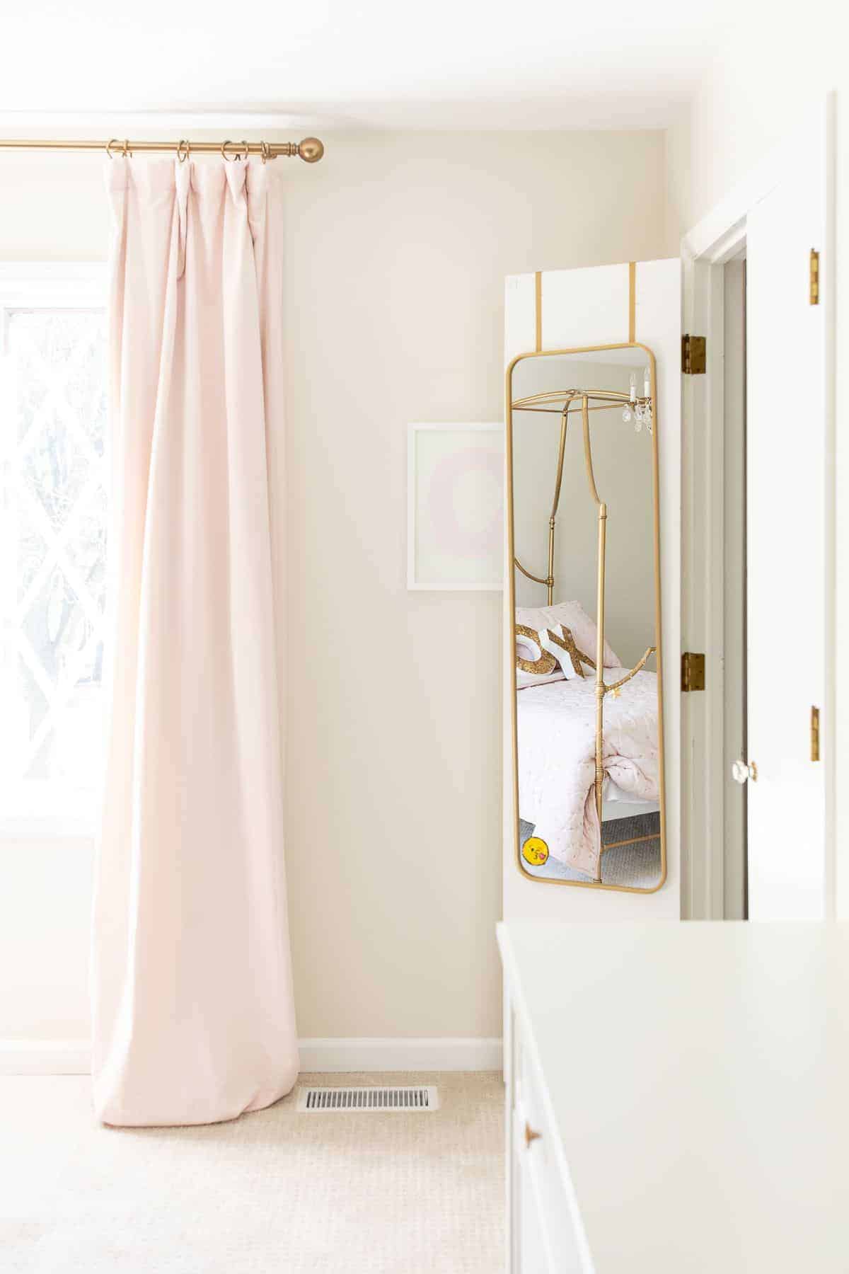 一个少女卧室，有粉红色的窗帘，衣柜门里面有一面金色的镜子。