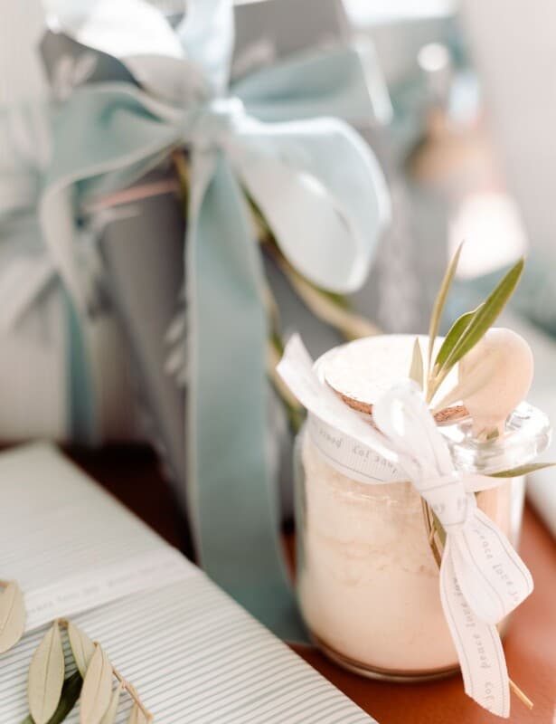 一个清楚的玻璃瓶子薄荷的牛奶浴配方在一棵树下与蓝色和被包裹的礼物。