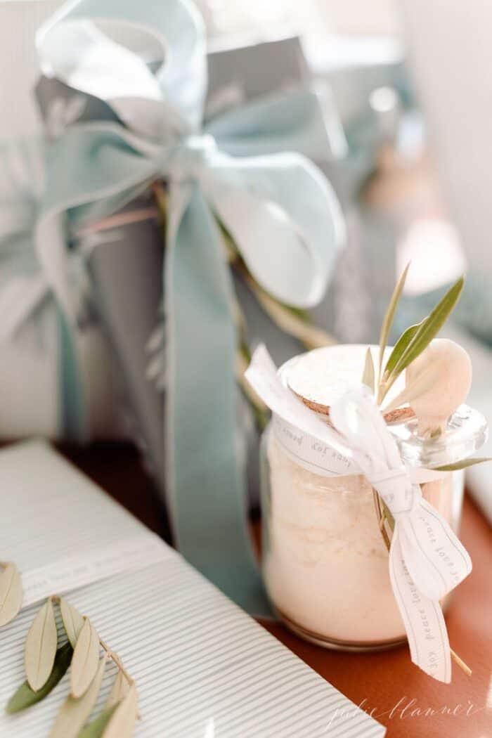 一罐透明的玻璃罐薄荷牛奶浴食谱，在树下，蓝色和包裹的礼物。