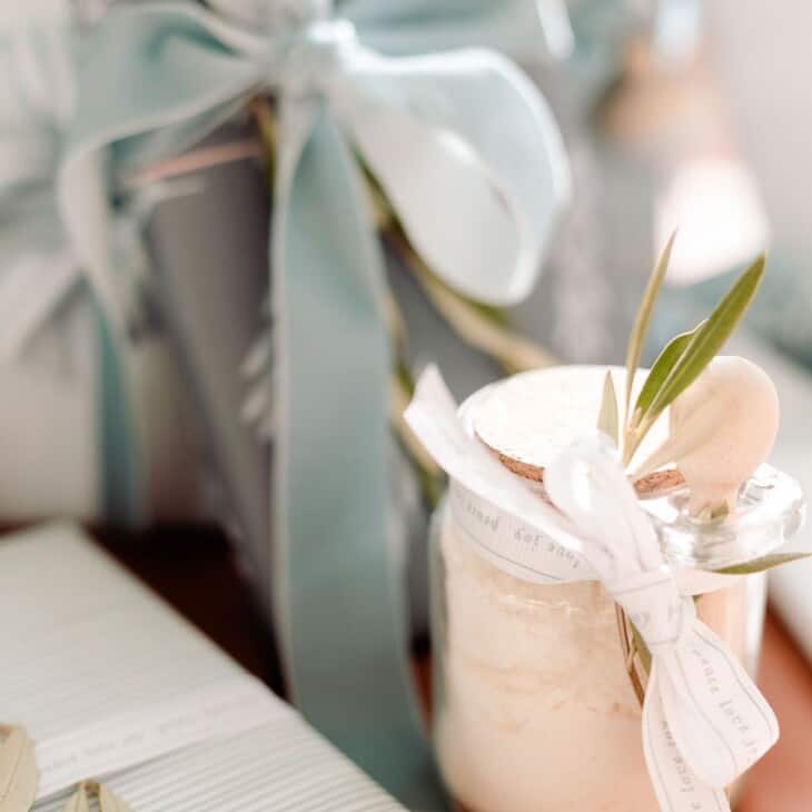 一罐透明的玻璃罐薄荷牛奶浴食谱，在树下，蓝色和包裹的礼物。