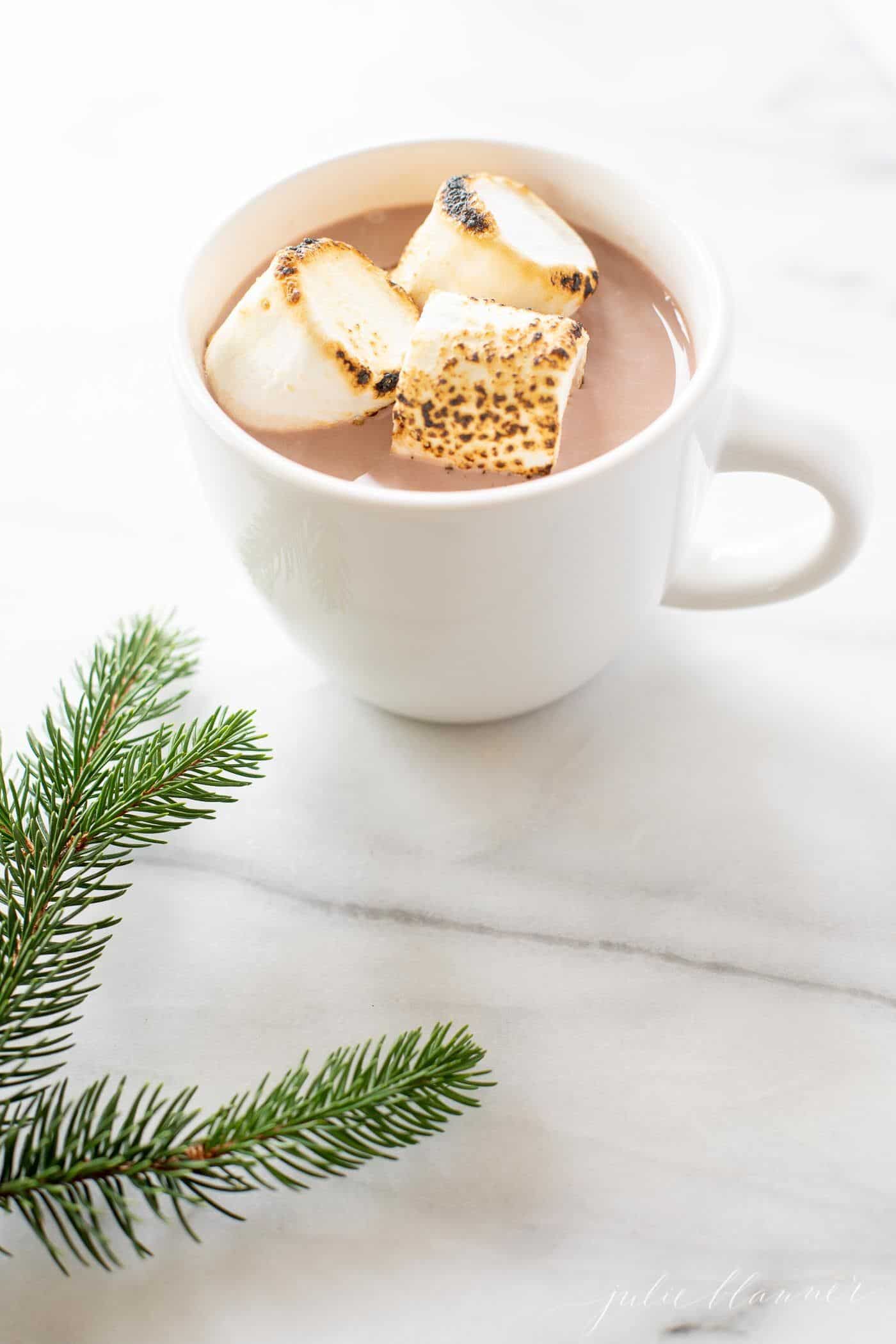 白色的杯子里装满了加了烈酒的热巧克力圣诞鸡尾酒，上面放着烤棉花糖。