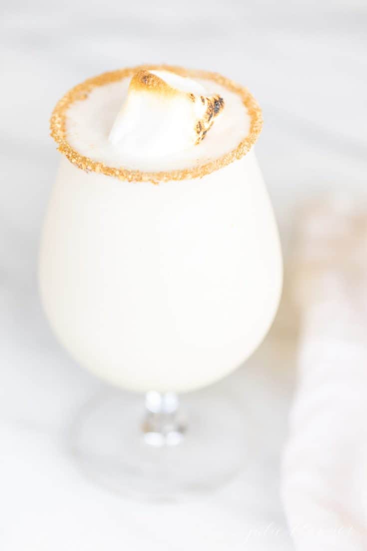 一个透明的高脚杯，盛满白色的圣诞鸡尾酒，顶部有棉花糖和糖边。