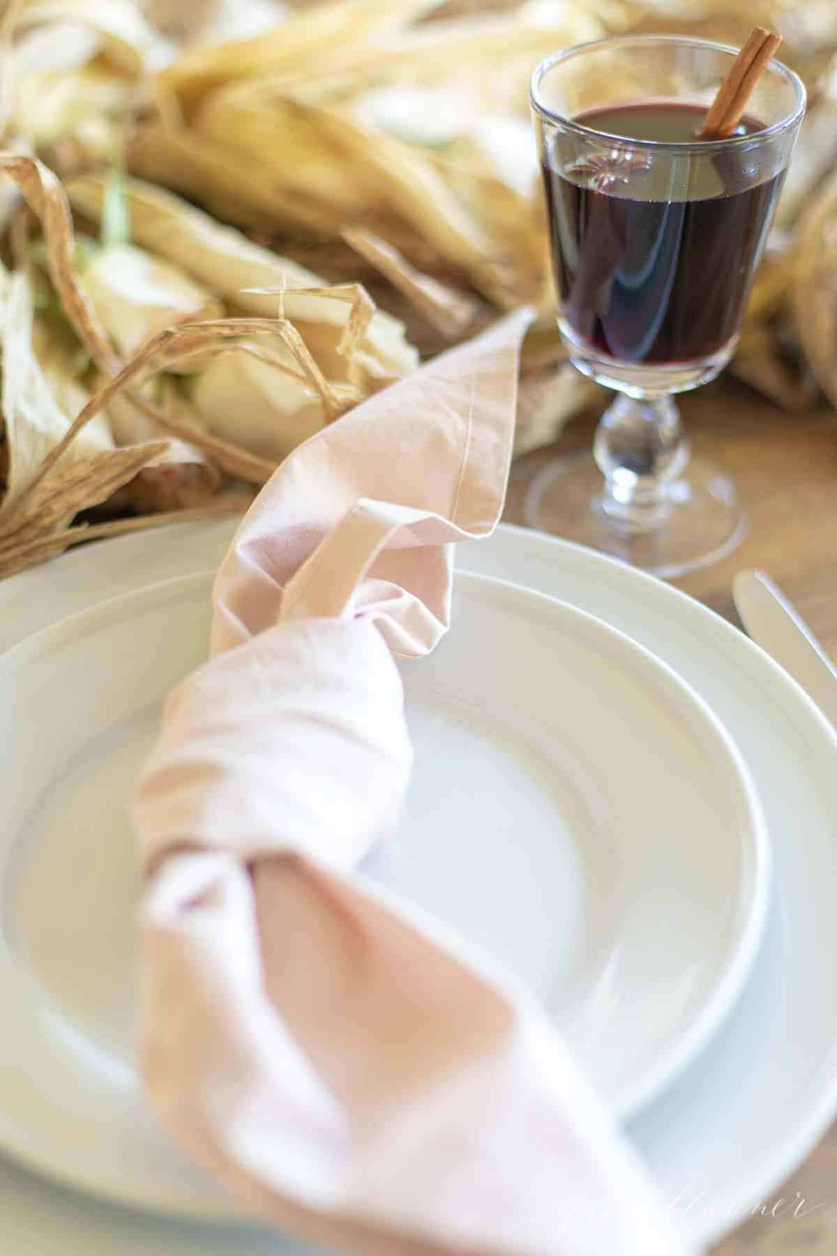 一杯装在透明玻璃杯里的感恩节鸡尾酒，旁边是白色的盘子和粉红色的餐巾。
