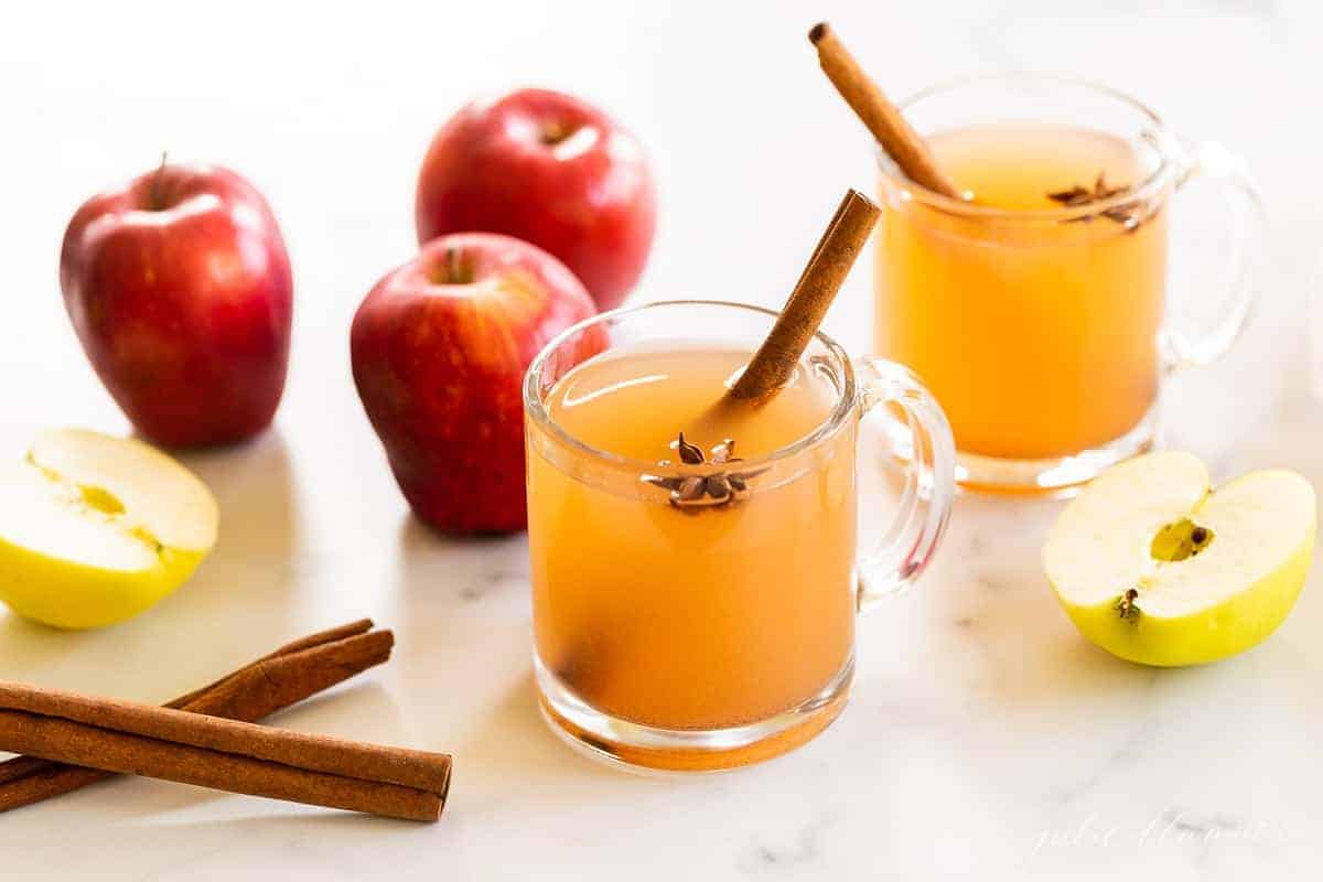 两个透明的杯子里装着苹果酒感恩节饮料，背景是苹果和肉桂棒。