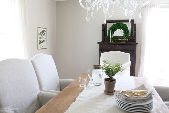 餐厅漆成Sherwin Williams易使用的米色，配有软垫白色椅子和一张木桌。