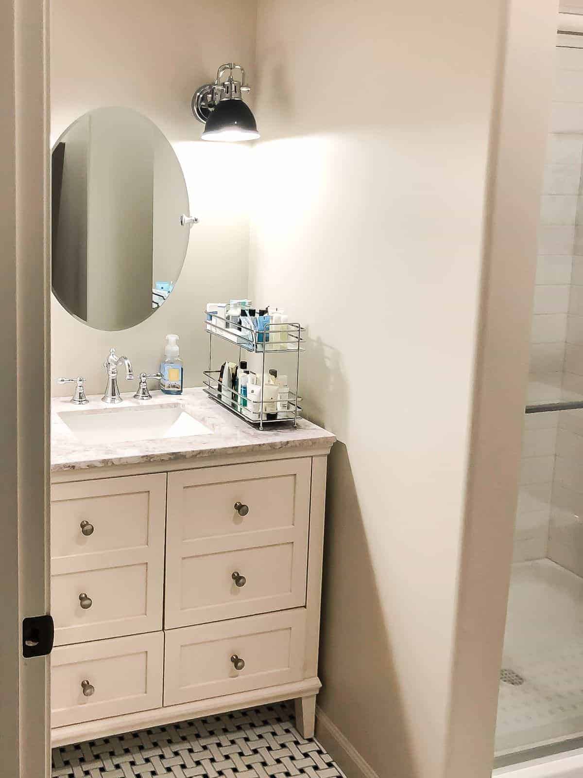 一间小浴室漆成舍温·威廉姆斯(sherwin williams)易于使用的米色，配有奶油色梳妆台和椭圆形镜子。