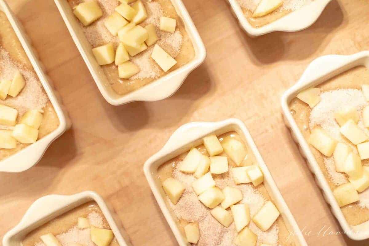 小的白色陶瓷面包锅装满苹果肉桂快速面包面糊。# applequickbreadgydF4y2Ba