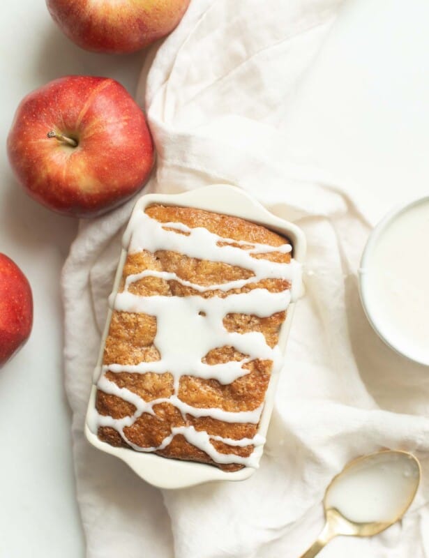 一个小面包的苹果面包，上面放着白色糖霜，周围是苹果和亚麻餐巾。