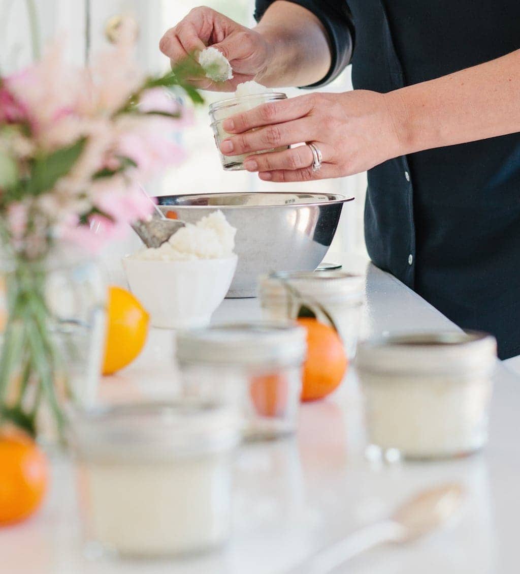 一个穿着黑色连衣裙的女人在不锈钢碗中搅动橙色糖磨砂膏食谱。