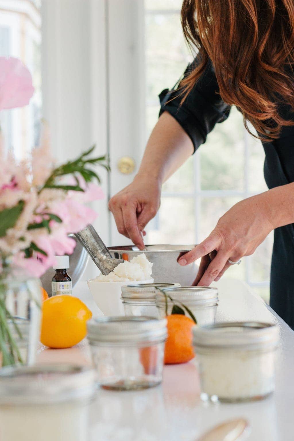 一个穿着黑色连衣裙的女人在不锈钢碗中搅动橙色糖磨砂膏食谱。