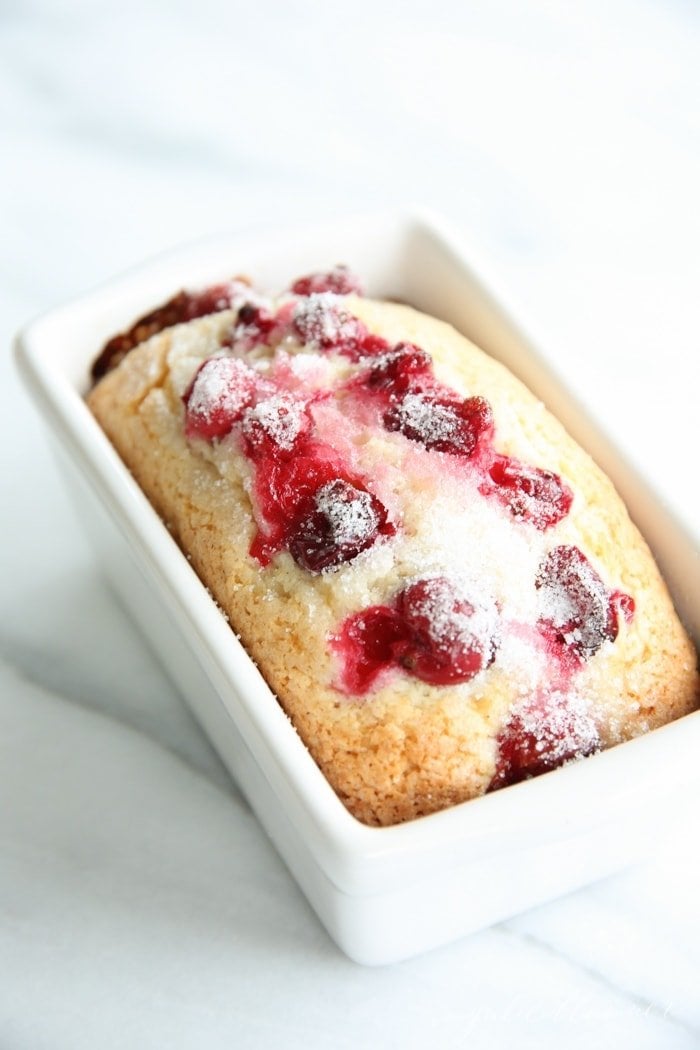 一条小面包，顶部有蔓越莓，在白色陶瓷面包盘中，白色背景。GydF4y2Ba