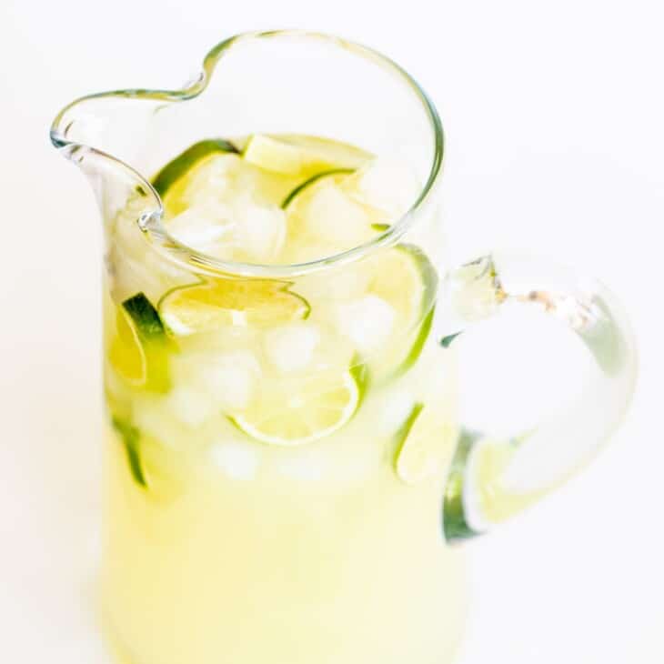 一个透明的玻璃投手，里面装满了自制的玛格丽塔酒，切成薄片的酸橙和冰。