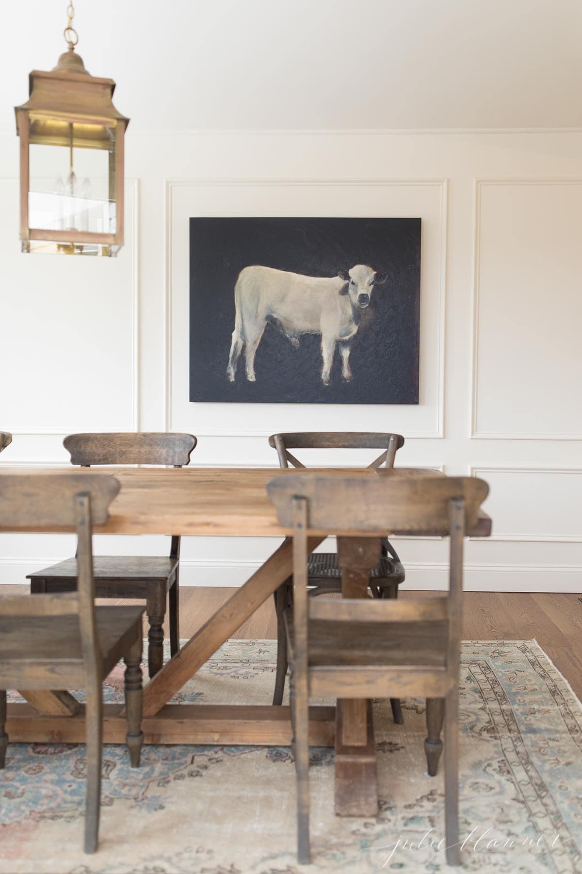 厨房旁边是一间白色的早餐室，有一张农场桌子，黄铜灯笼，背景是一幅奶牛的画。
