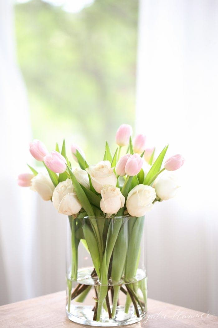 一个透明的花瓶，装满了玫瑰和郁金香的复活节桌子装饰安排