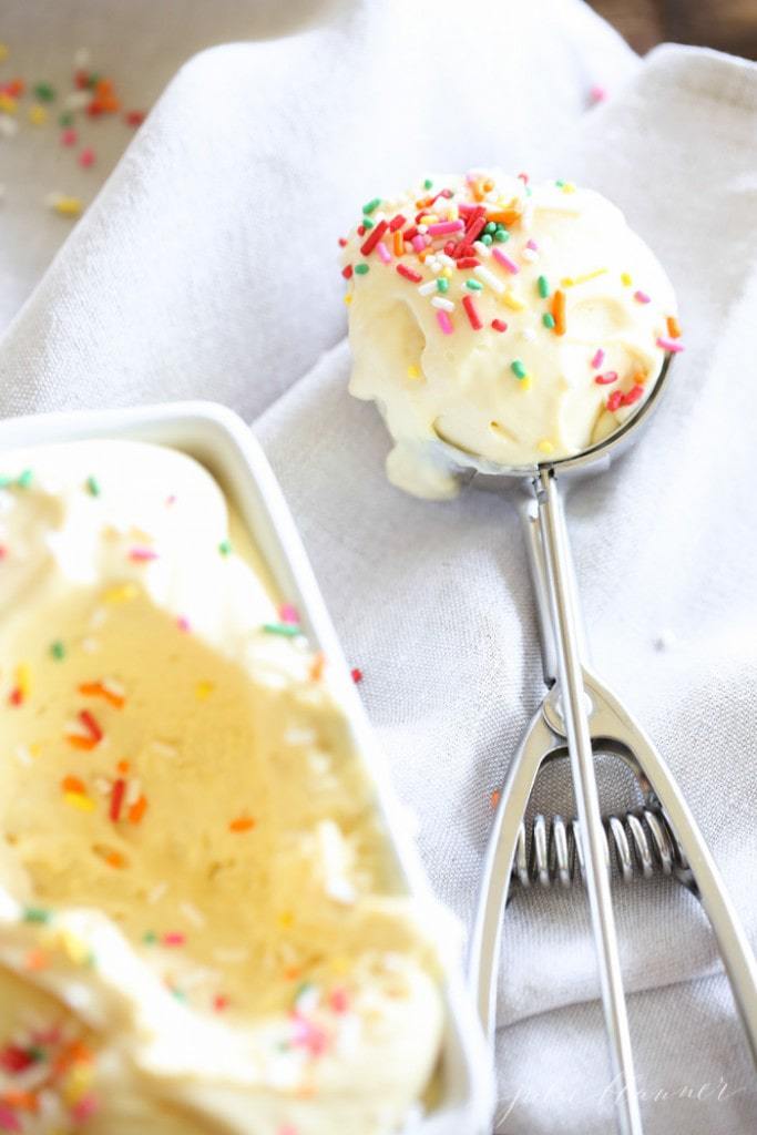 一个白色的面包平底锅，里面装满了自制的冰淇淋，边上放着一勺冰淇淋，上面撒满了冰淇淋屑。