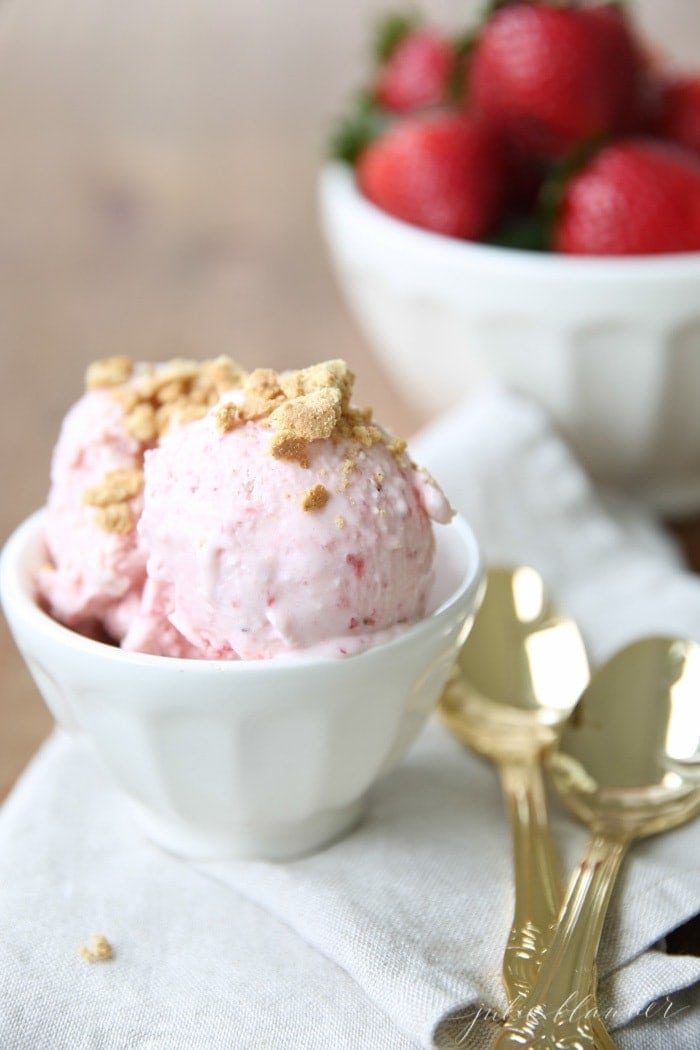 一个白色的碗，里面放着一个没有搅拌器的冰淇淋配方，金色的勺子和草莓放在一边。