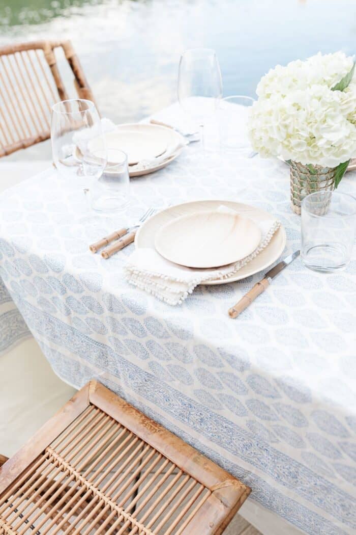 一个露天的餐桌，白色的花朵和蓝白相间的桌布，水为背景。