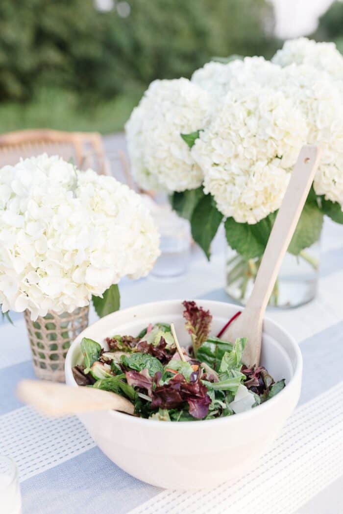白色绣球花花瓶旁边的沙拉碗设置了户外晚餐