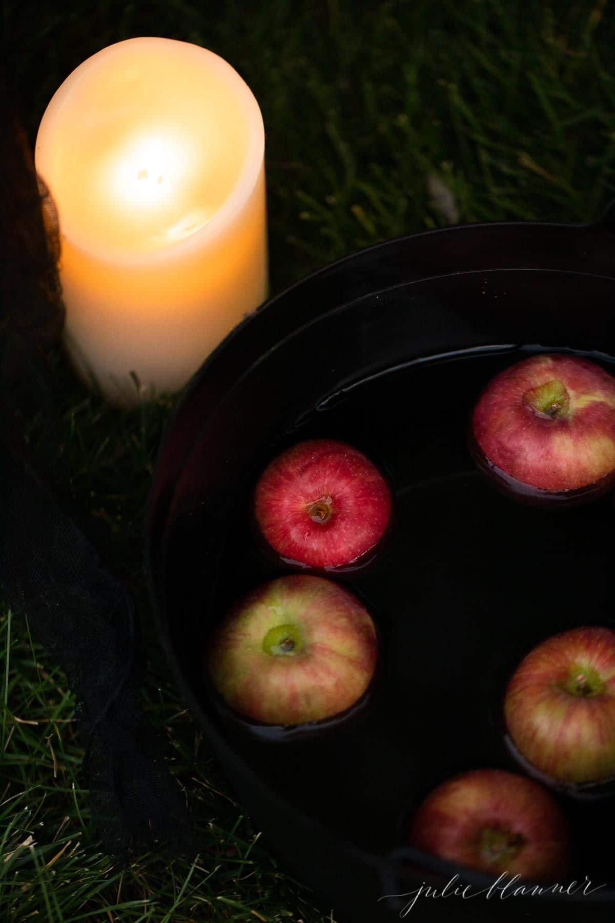 一块充满新鲜苹果的大锅和一个电池动力的柱子蜡烛坐在草地上。