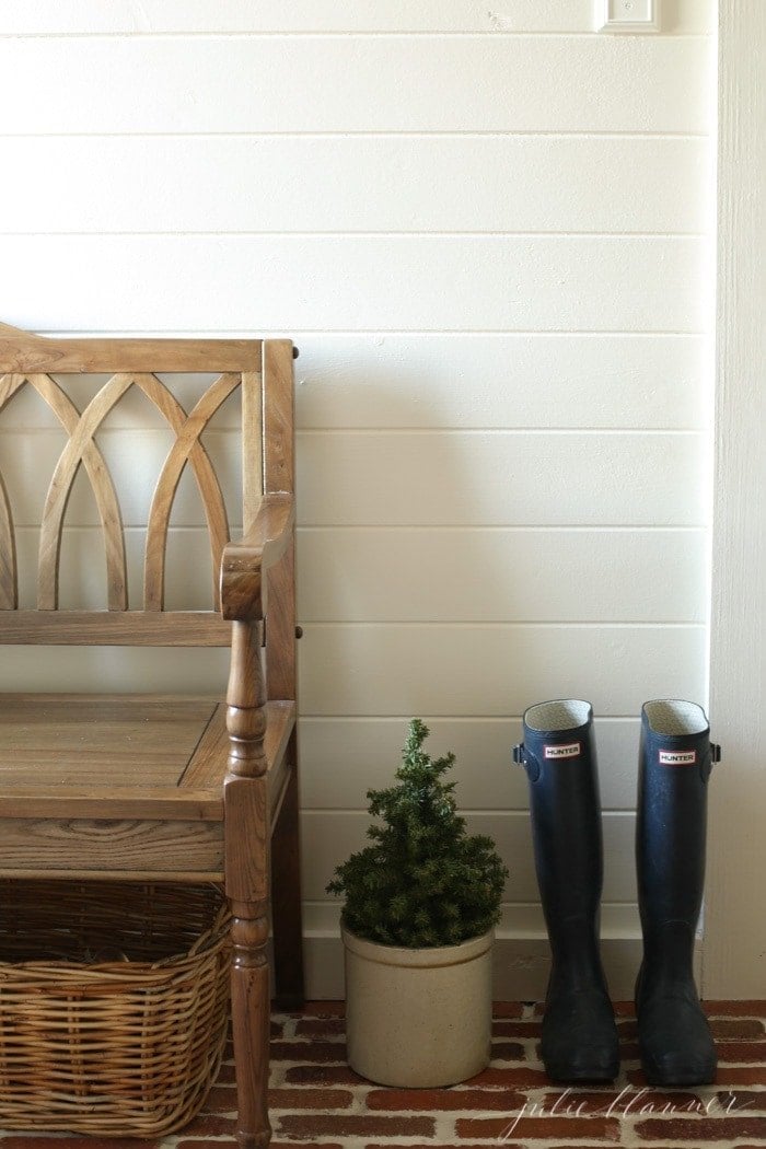 一个白色镶板的泥室，带有薄砖地板和木凳。