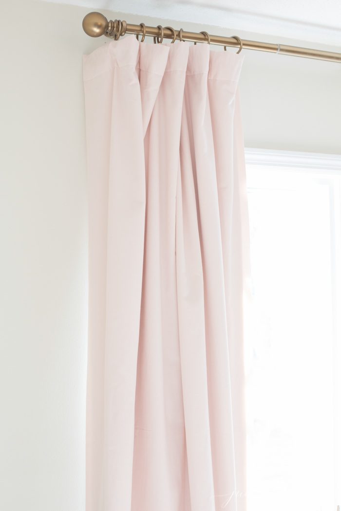 淡粉色天鹅绒遮光窗帘映衬着白色的墙壁。