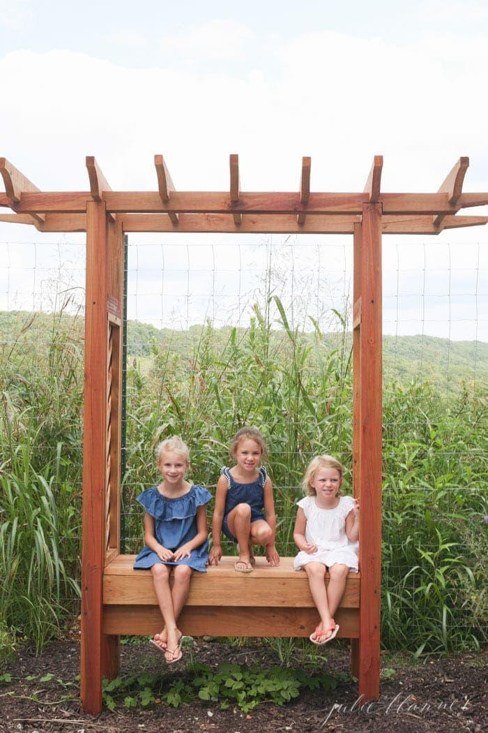 三个小女孩坐在花园的长凳上，身后是草。