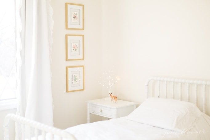 一个白人女孩的卧室，白色遮光窗帘和金框艺术品。