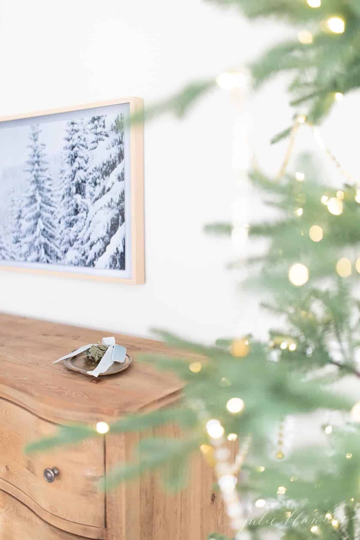 一间卧室的墙上挂着一台三星艺术电视，展示着冬天的景色，前景是一棵圣诞树。