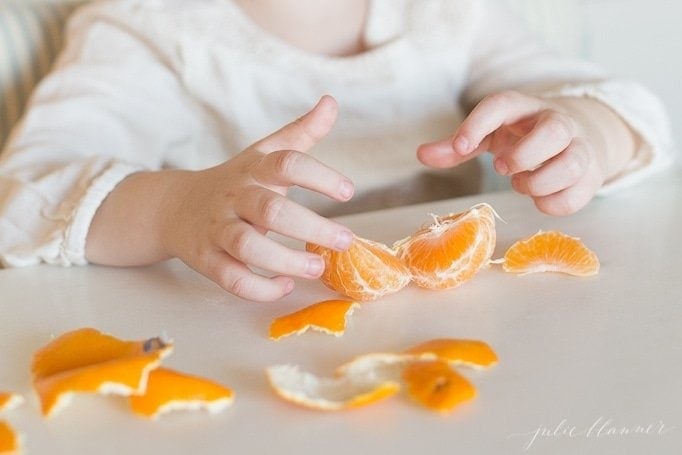 一个孩子的手在白色的工作台上剥橘子。gydF4y2Ba
