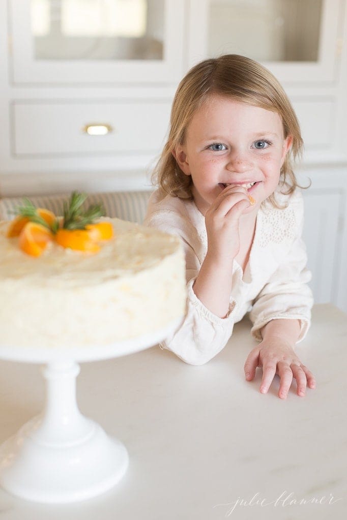 图片的前景是一个小女孩吃着一个自制的桔子蛋糕。gydF4y2Ba