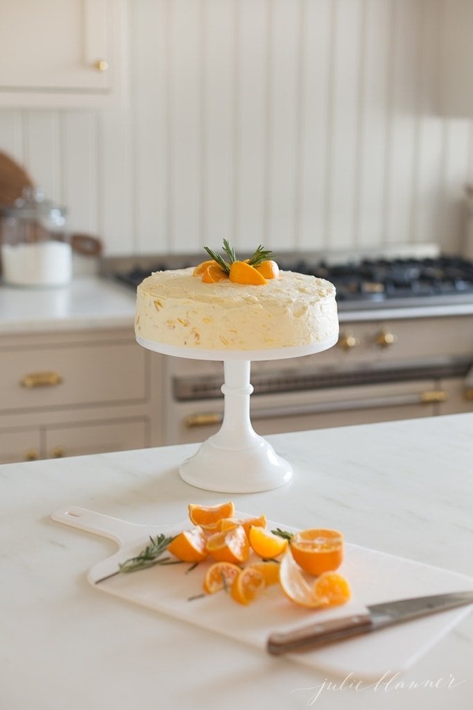 白色蛋糕架上的圆形磨砂猪蛋糕，前景是切好的桔子片。gydF4y2Ba