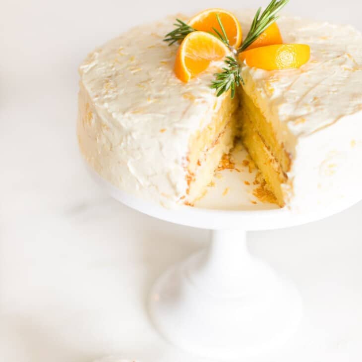 一个圆形的普通话橙色蛋糕，切成薄片，放在白色蛋糕基座上。