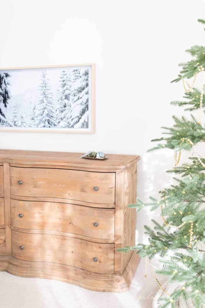 一台三星艺术电视在卧室的墙壁上展示了一个冬季场景，前景中有圣诞树。