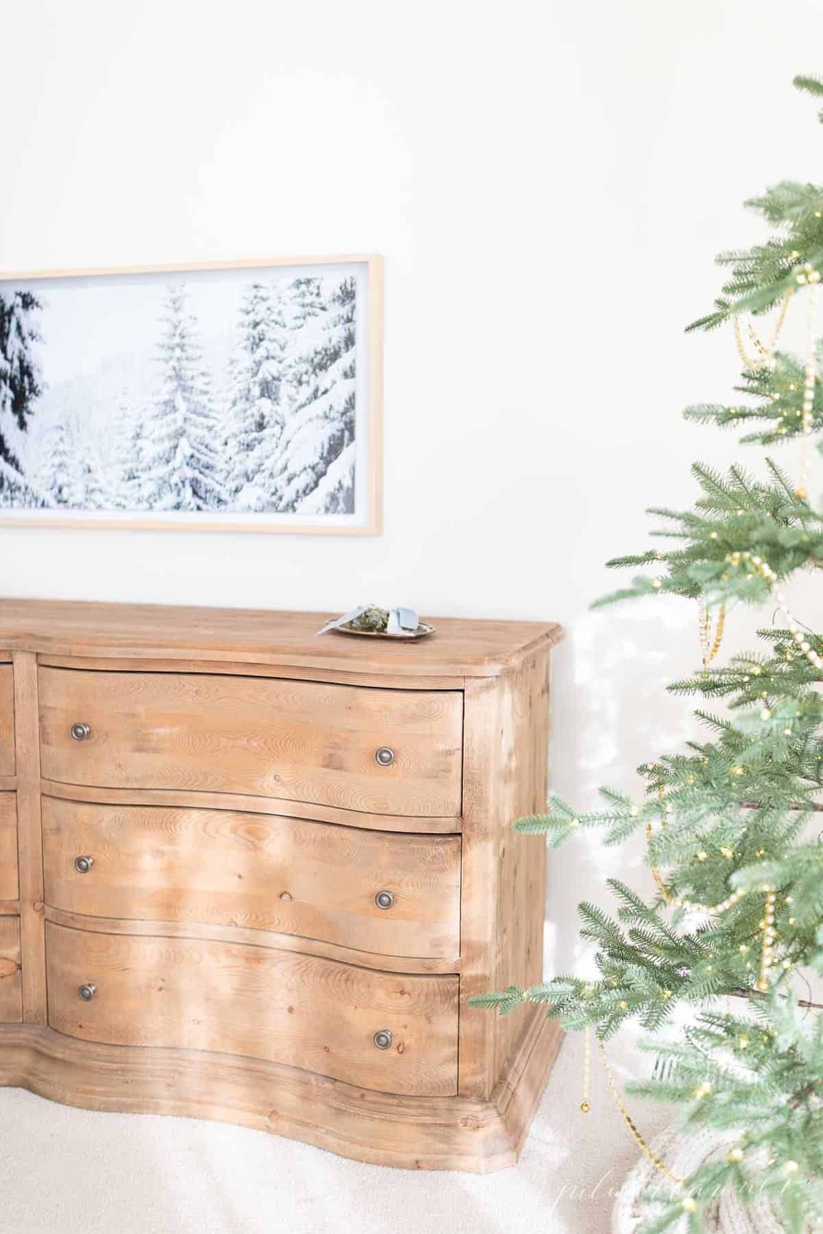 一间卧室的墙上挂着一台三星艺术电视，展示着冬天的景色，前景是一棵圣诞树。