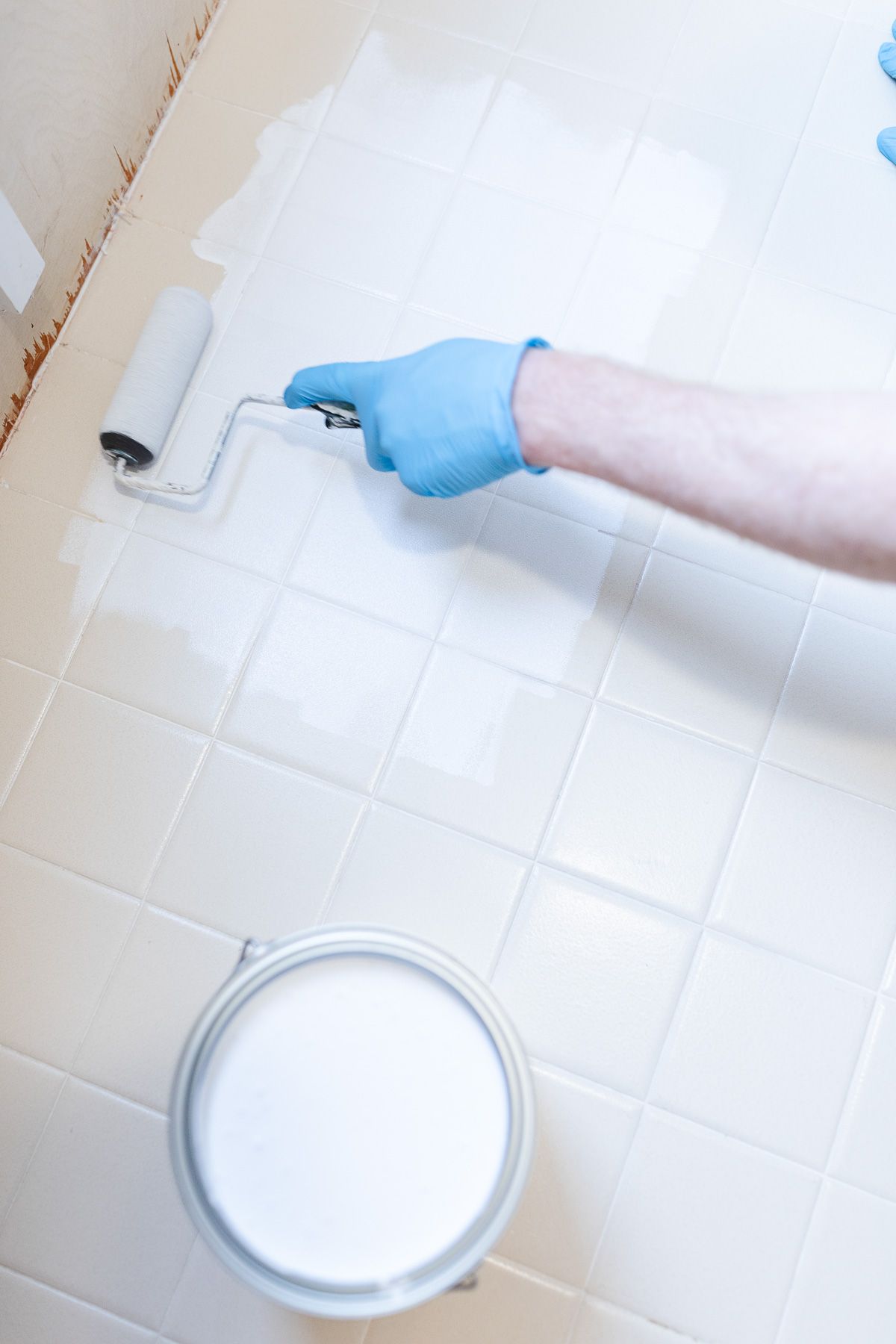 一个戴着乳胶手套的人在旧浴室瓷砖上滚动处理剂