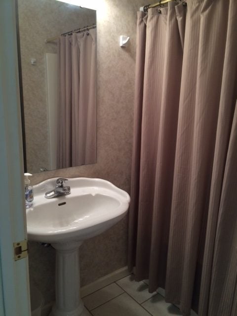 一个过时的浴室，带有棕褐色的墙纸，基座水槽。